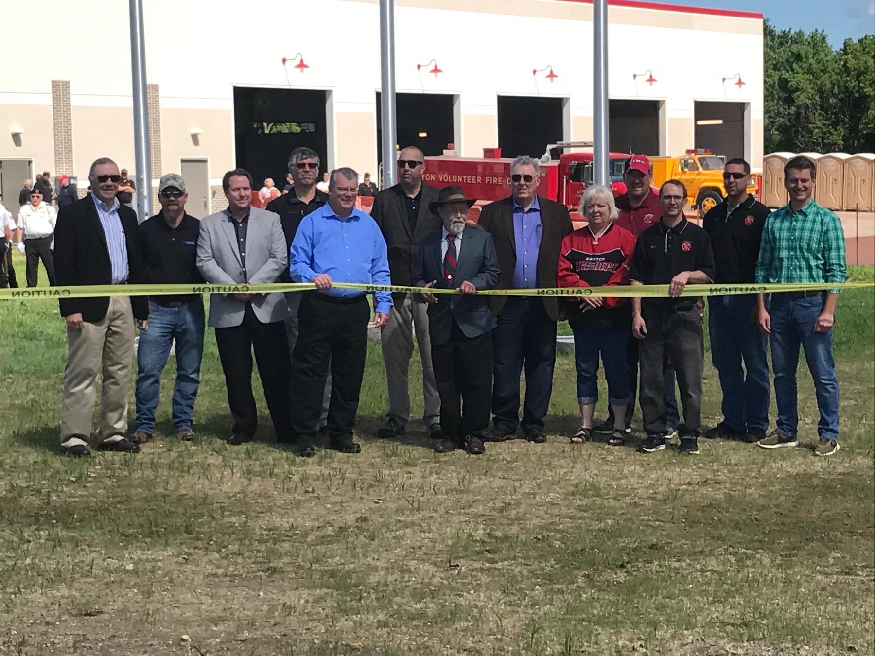 Kenyon fire officers and the city council cutting the ribbon at the new station in June 2017, with two of the department's trucks in the bays behind them